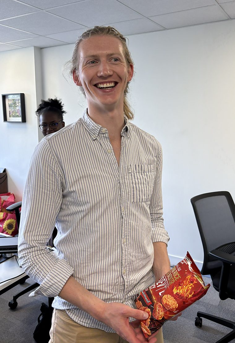 Richard from Innovate Heat laughing while holding an open packet of Devil Spicy rice crackers in his office